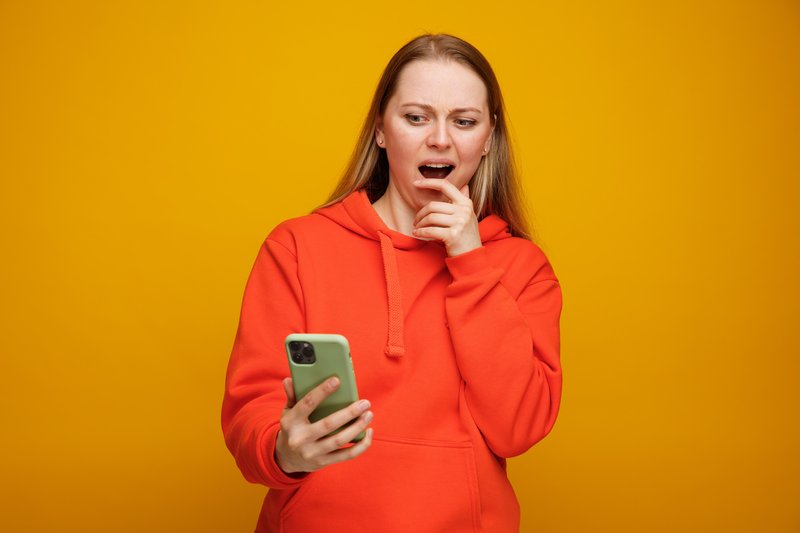 concerned-young-blonde-woman-holding-looking-mobile-phone-keeping-hand-chin