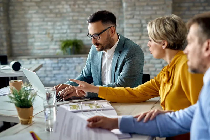 financial-advisor-working-computer-while-having-meeting-with-couple-office